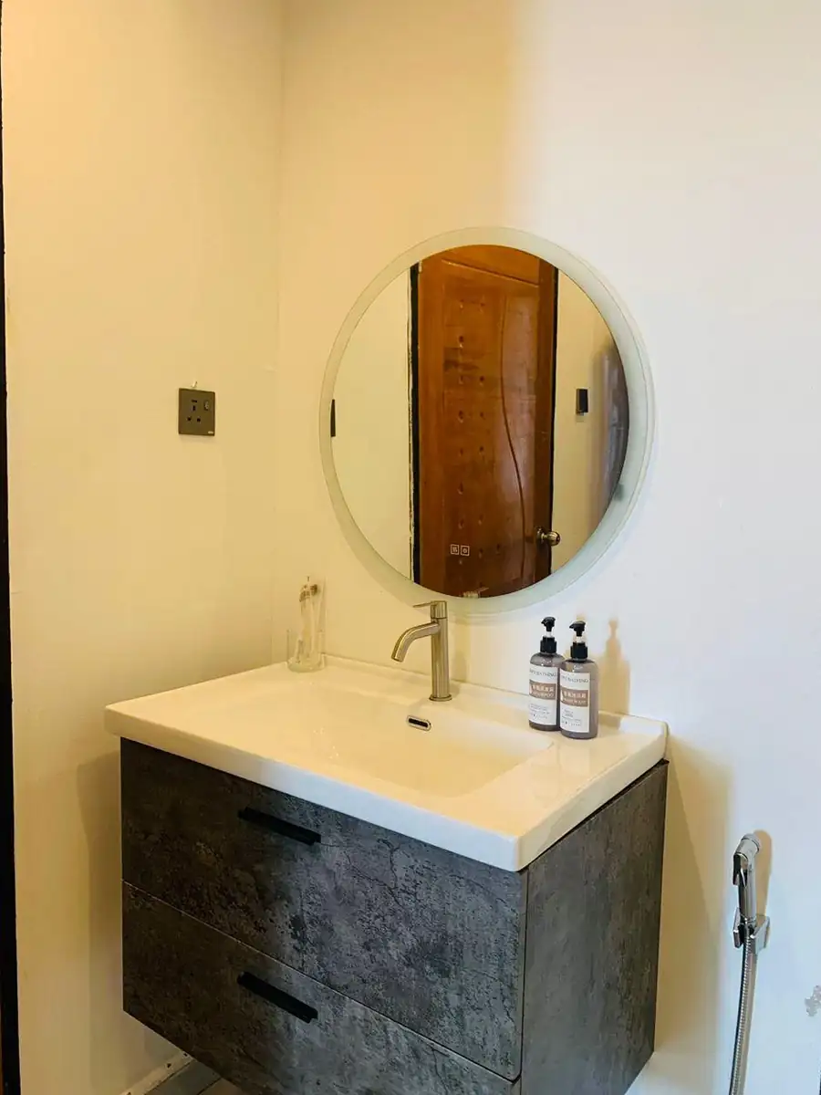 Modern bathroom vanity inside the Bedroom Deluxe 1 Bed at Turtle Seaweed Resort featuring a textured grey floating cabinet and a round backlit mirror.